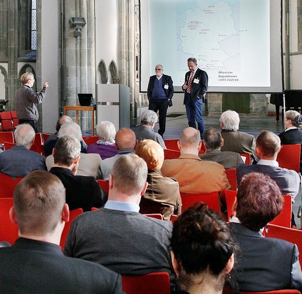 Man sieht die Diskussion nach dem Vortrag von Professo Doktor Christian Peters. Vor der Leindwand stehen der Redner und Professor Wilfried Reininghaus