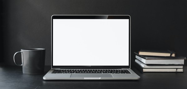 Ein Laptop mit weißem Bildschirm, links daneben eine schwarze Tasse und rechts ein Bücherstapel