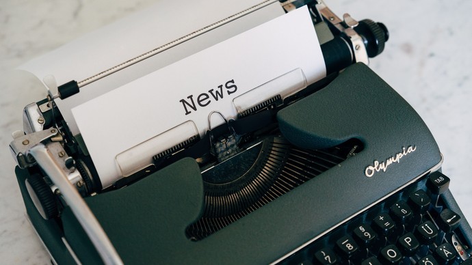 Auf dem Bild sehen wir eine grüne, antike Schreibmaschine mit eingespanntem Papier auf dem das Wort News steht Auf dem Bild sehen wir eine grüne, antike Schreibmaschine mit eingespanntem Papier auf dem das Wort News steht