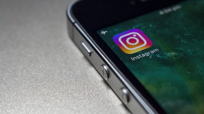 Auf dem Bild sehen wir rechts oben ein Smartphone, dass auf einem silbernen Untergrund liegt. Auf dem Display befindet sich das Instagram Logo Auf dem Bild sehen wir rechts oben ein Smartphone, dass auf einem silbernen Untergrund liegt. Auf dem Display befindet sich das Instagram Logo